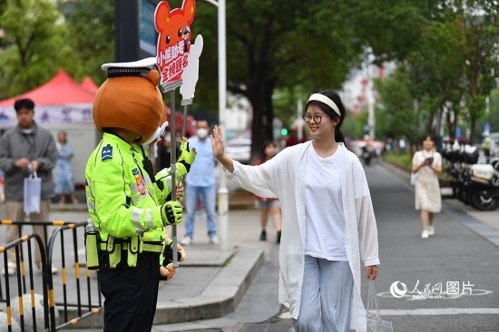 6月7日上午9時(shí)，隨著鈴聲的響起，2023年江西高考正式開考，江西省的53.57萬考生以縣（區(qū)）為單位隨機(jī)安排在全省256個(gè)考點(diǎn)、18968個(gè)考場(chǎng)參加高考。圖為“小熊交警”和考生擊掌鼓勵(lì)。 人民網(wǎng)記者 時(shí)雨攝