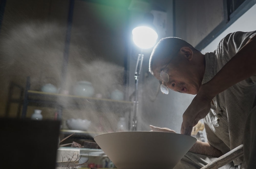 ↑ 在景德鎮(zhèn)，手工匠人吹去坯內(nèi)的泥土（2021年7月14日攝）。