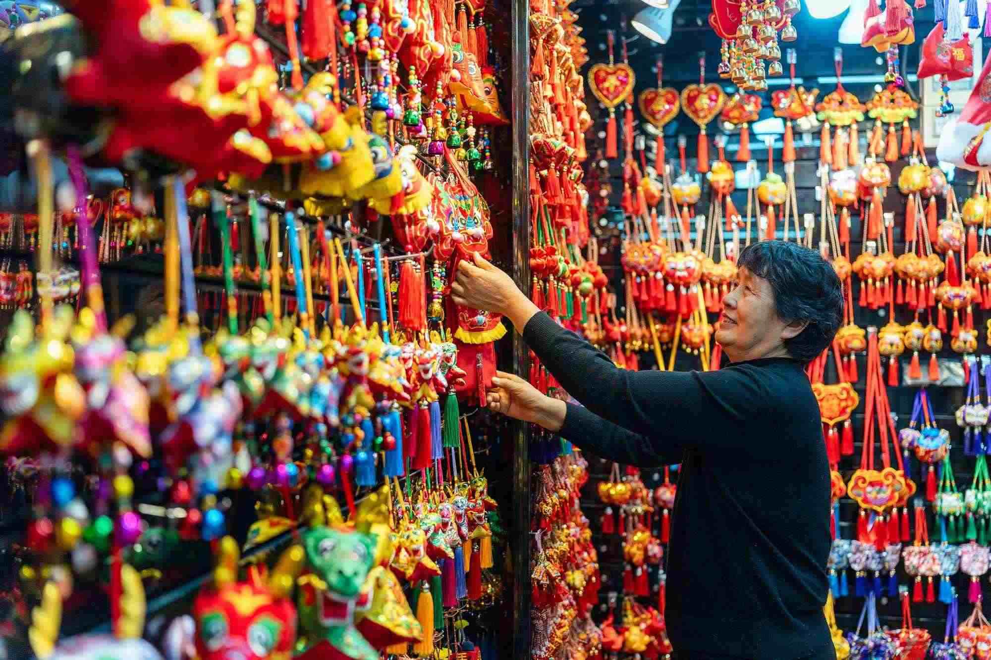 2023年12月11日，金華義烏國際商貿(mào)城，龍年喜慶用品掛滿攤位，顧客正在挑選中。