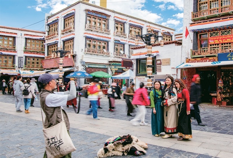 千年八廓街，見(jiàn)證民族團(tuán)結(jié)。2021年7月，習(xí)近平總書(shū)記來(lái)到位于西藏拉薩老城區(qū)的八廓街，感慨地說(shuō)：“千年八廓街，是我們各民族建起來(lái)的八廓街。各民族文化在這里交流交往交融，我們中華民族的大家庭在這里其樂(lè)融融?！眻D為2023年6月13日，游客身著藏裝在八廓街拍照留念。 新華社記者 姜帆/攝