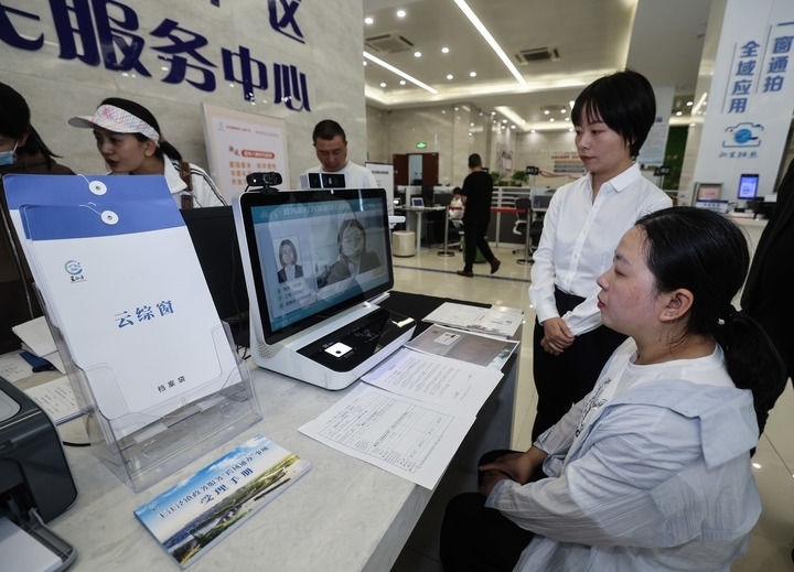 在浙江省嘉興市秀洲區(qū)王江涇鎮(zhèn)便民服務(wù)中心的“跨域通辦·云綜窗”窗口，辦理開業(yè)登記的個(gè)體工商戶（右一）通過(guò)該系統(tǒng)與江蘇省蘇州市吳江區(qū)盛澤鎮(zhèn)行政審批局工作人員視頻連線，進(jìn)行身份讀取及材料線上審核（2024年5月9日攝）。新華社記者 徐昱 攝