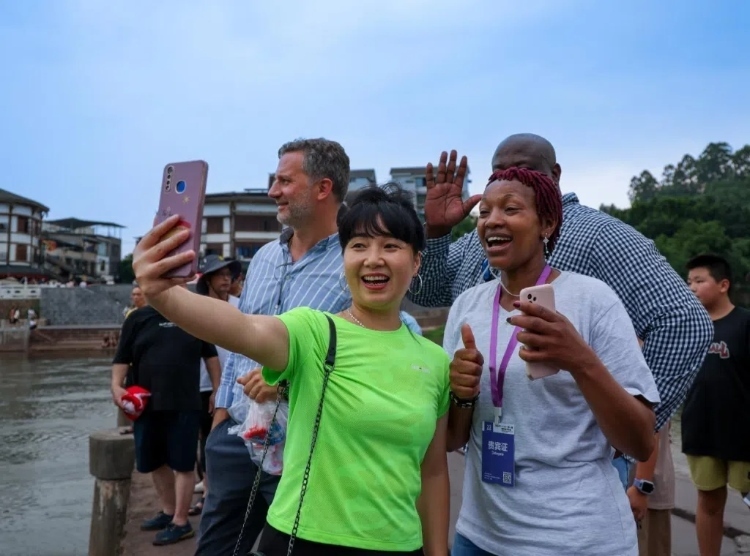 2024“一帶一路”媒體合作論壇聯(lián)合采訪調(diào)研行成員在樂山蘇稽古鎮(zhèn)與游客合影留念。本報記者 伊霄攝