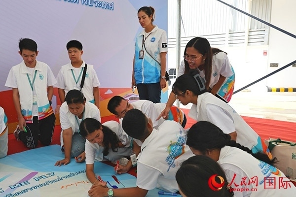 泰國學(xué)生在開營儀式展板上繪制圖案。人民網(wǎng)記者 白元琪攝