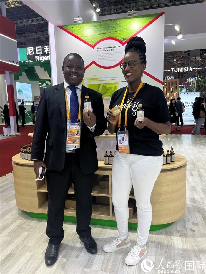 6月6日，布隆迪駐華大使館一等參贊布利馬索·阿爾弗雷德 (左，Bulimaso Alfred) 和參展商卡馬里扎·埃斯特拉 (Kamariza Estella) 在第七屆中國國際進口博覽會布隆迪館展示當(dāng)?shù)厣a(chǎn)的辣木油。（人民網(wǎng) 艾里士 攝）