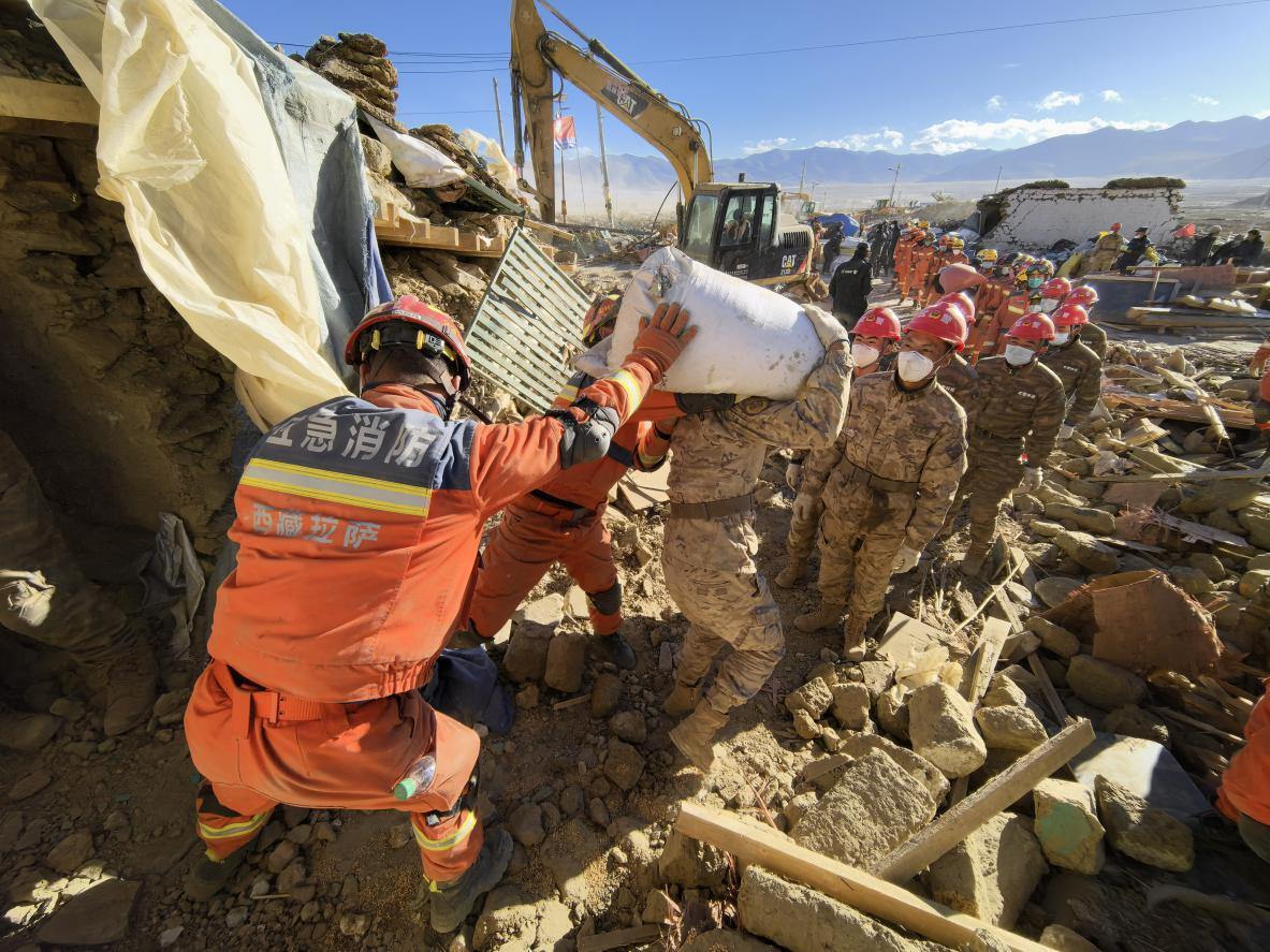 1月11日，定日縣長所鄉(xiāng)古榮村，應急消防等救援人員排隊接力搶運掩埋在倒塌房屋下的群眾財物。人民日報記者楊翹楚攝