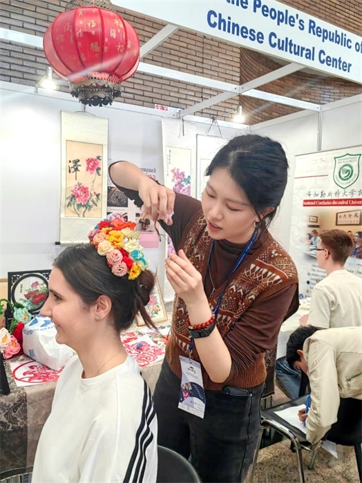 展覽正值羅馬尼亞迎春花節(jié)，國(guó)際中文教師志愿者潘婧穎向游客們介紹了國(guó)家非物質(zhì)文化遺產(chǎn)——福建泉州的簪花文化。布加勒斯特大學(xué)孔子學(xué)院供圖。